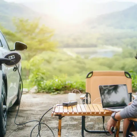 Foto, das ein Elektrofahrzeug zeigt, das einen Laptop mit einem V2L-Kabel auflädt